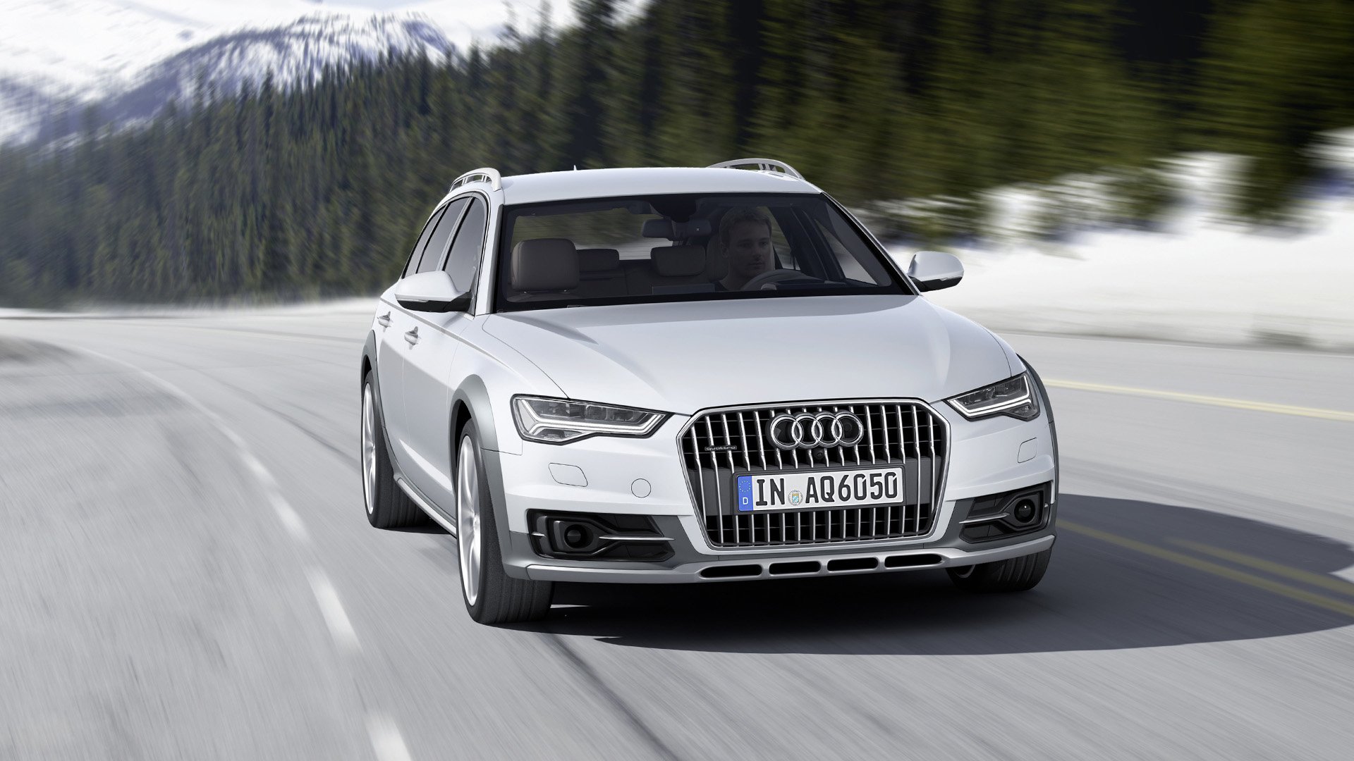 Vit Audi A6 Allroad på landsväg med snöig bakgrund.