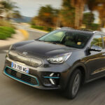 Mörkgrå Kia e-Niro kör på väg sedd snett framifrån.