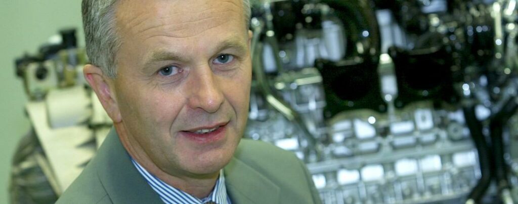 En man i kostym och slips står framför en bil. (AI text)