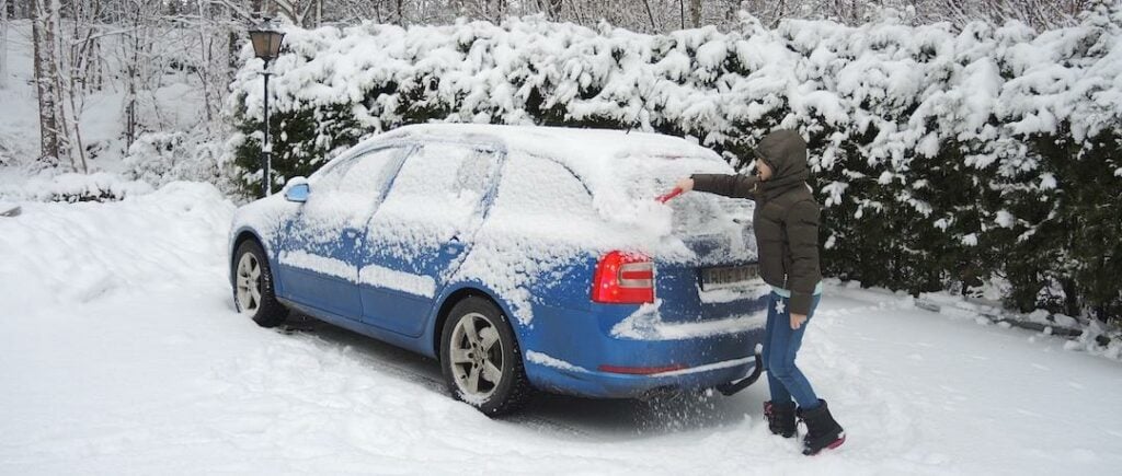 En kvinna rengör sin bil i snön. (AI text)