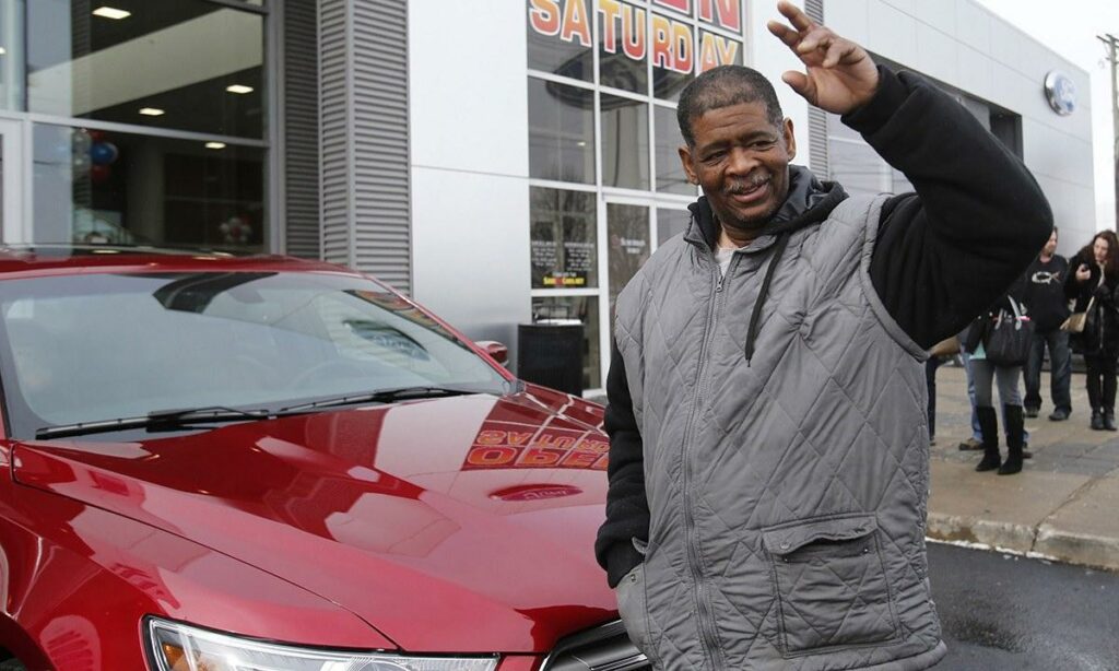 En man vinkar till kameran framför en Ford-handlare. (AI text)