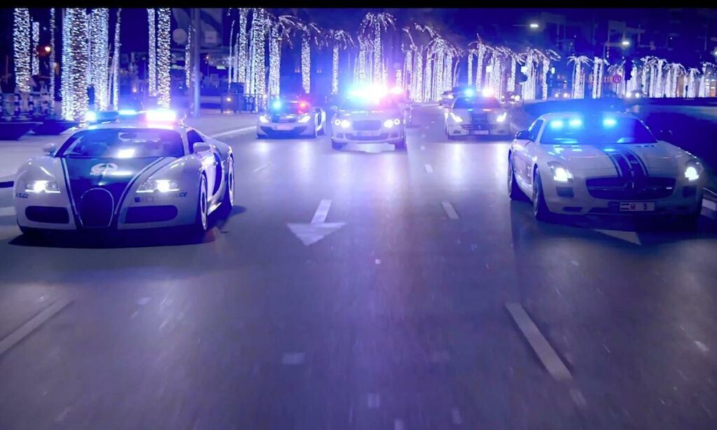 En polisbil kör nedför en gata med sirener och strålkastare tända. (AI text)