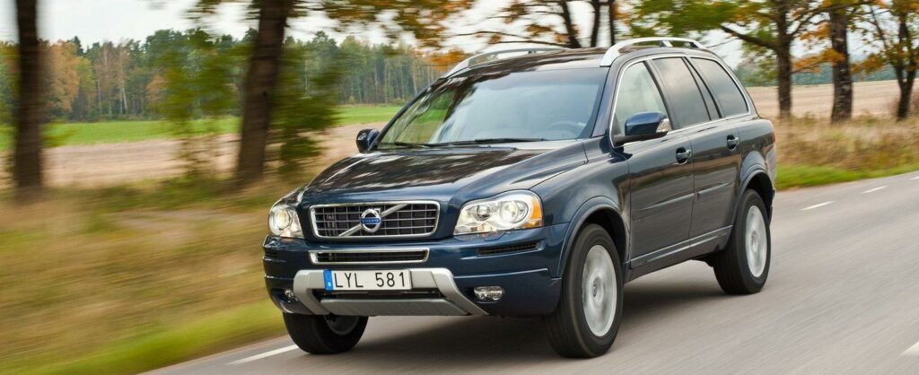 En Volvo XC90 SUV kör nerför en landsväg. (AI text)