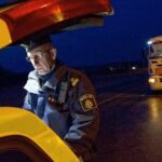 En polisstående står bredvid en gul bil på natten. (AI text)