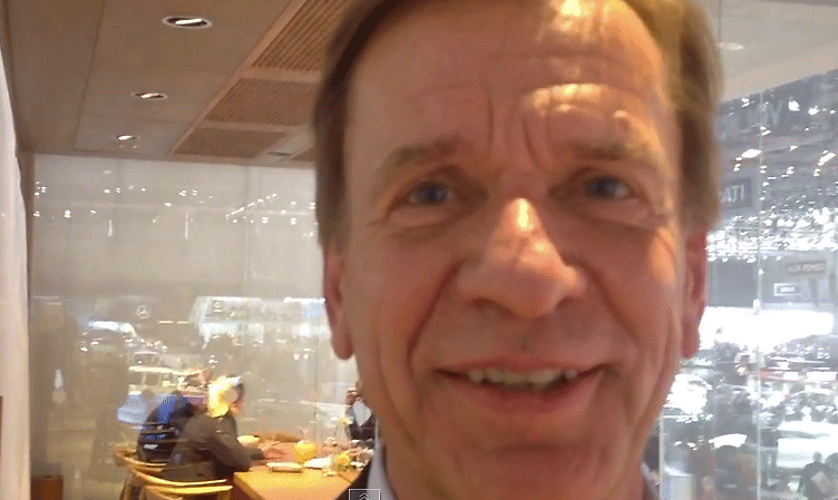 En man i kostym och slips leder glatt mot kameran. (AI text)