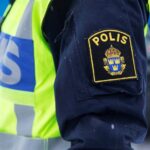 En polis i ett gult västar står framför en bil. (AI text)
