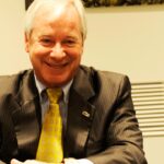 En man i kostym och slips sitter vid en bordet. (AI text)