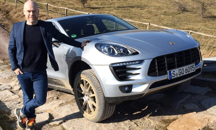 En man står bredvid en Porsche Macan. (AI text)