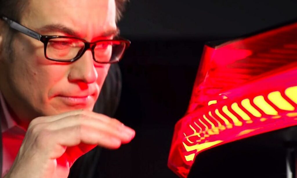 En man i glasögon tittar på en röd bil. (AI text)