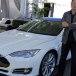 En man står bredvid en vit Tesla Model S. (AI text)