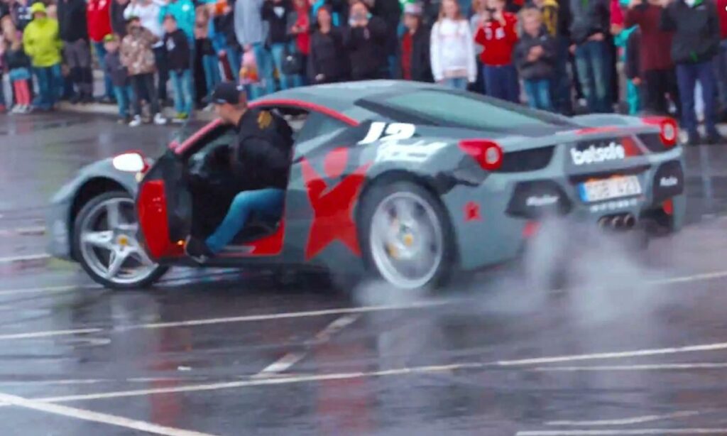 En Ferrari F12tdf kör nedför en gata med åskådare som tittar på. (AI text)