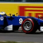 En blå och gul formelbil kör på banan. (AI text)