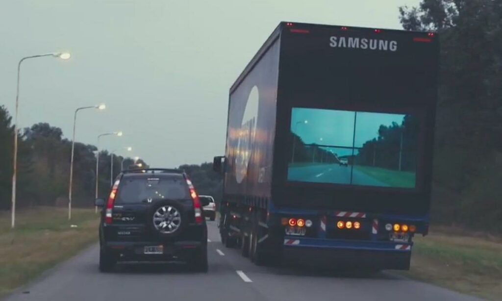 En lastbil kör nedför en väg med en stor skärm. (AI text)