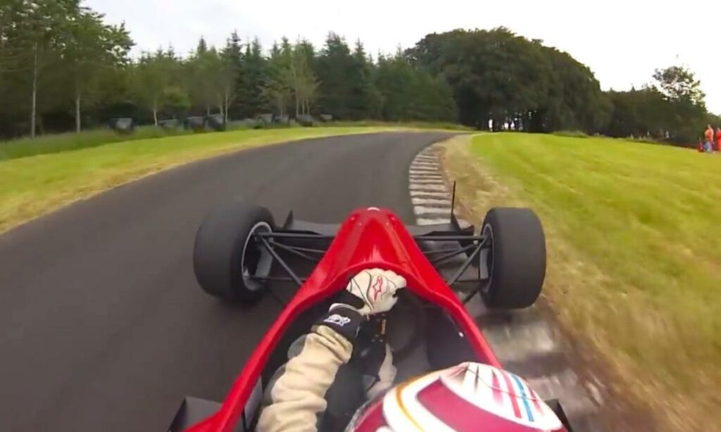 En röd racerbil kör längs banan. (AI text)