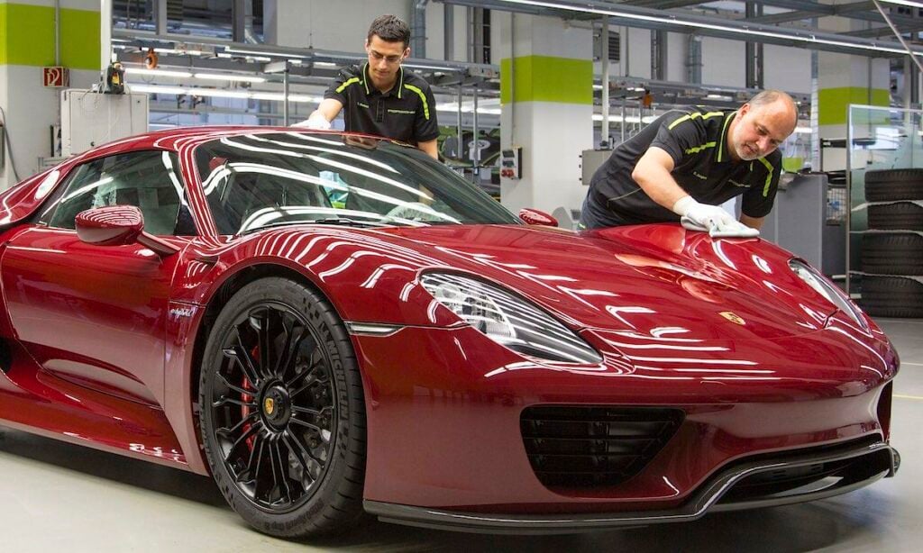 En man arbetar med en röd sportbil i en fabrik. (AI text)