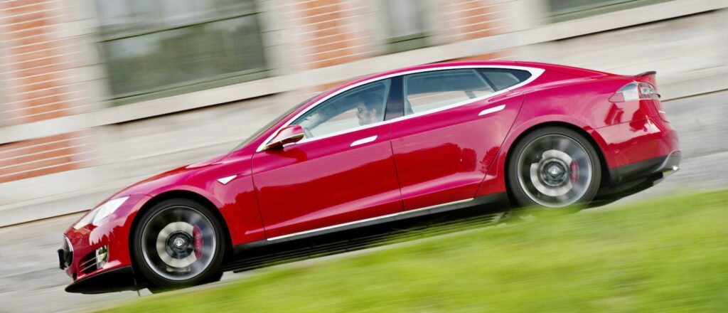 En röd Tesla Model S kör ner en gata. (AI text)