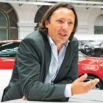 En man i kostym sitter vid en bord i förväg av en bil. (AI text)