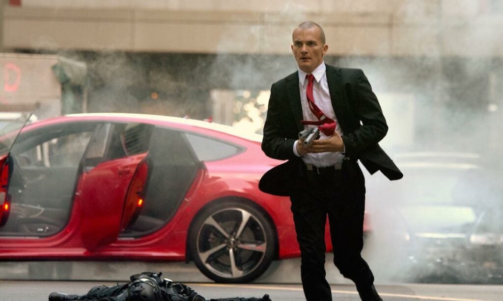 En man i kostym går förbi en röd bil. (AI text)