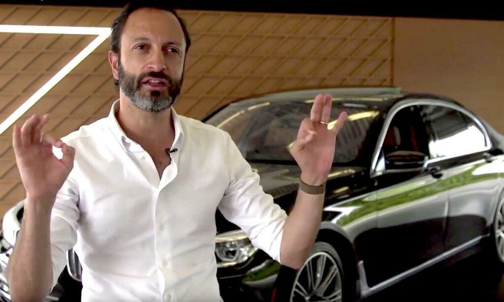 En man i ett vitt skjortäpplek står bredvid en BMW. (AI text)