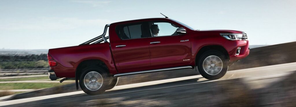 En röd Toyota Hilux kör nerför en backe. (AI text)