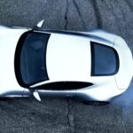 En vit sportbil kör nerför en gata. (AI text)