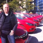 En man står bredvid en rad röda bilar. (AI text)