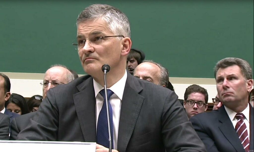 En man i kostym och slips sitter vid en bord med en dator. (AI text)