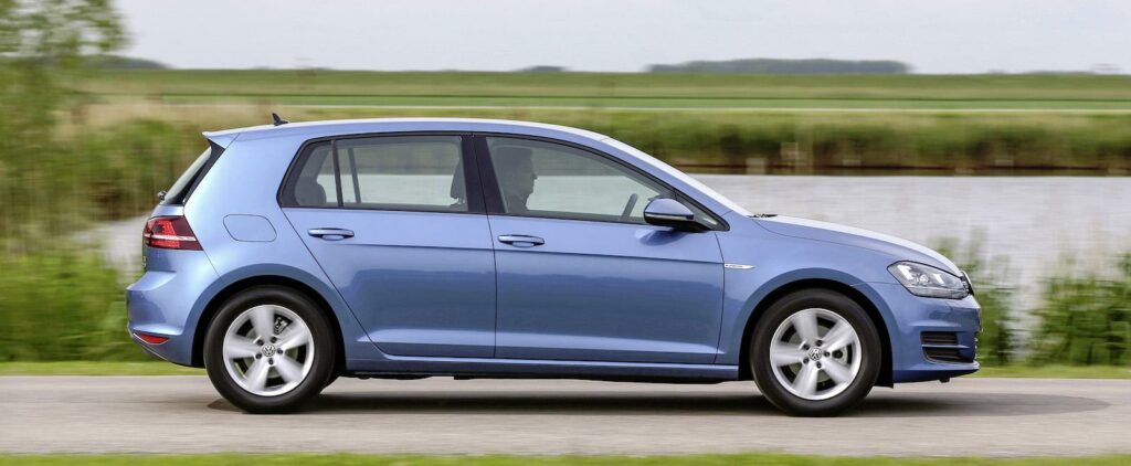 En blå Volkswagen Golf GTI kör längs en landsväg. (AI text)