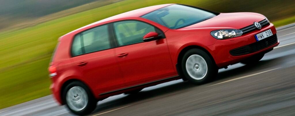 En röd Volkswagen Golf kör på en blöt väg. (AI text)