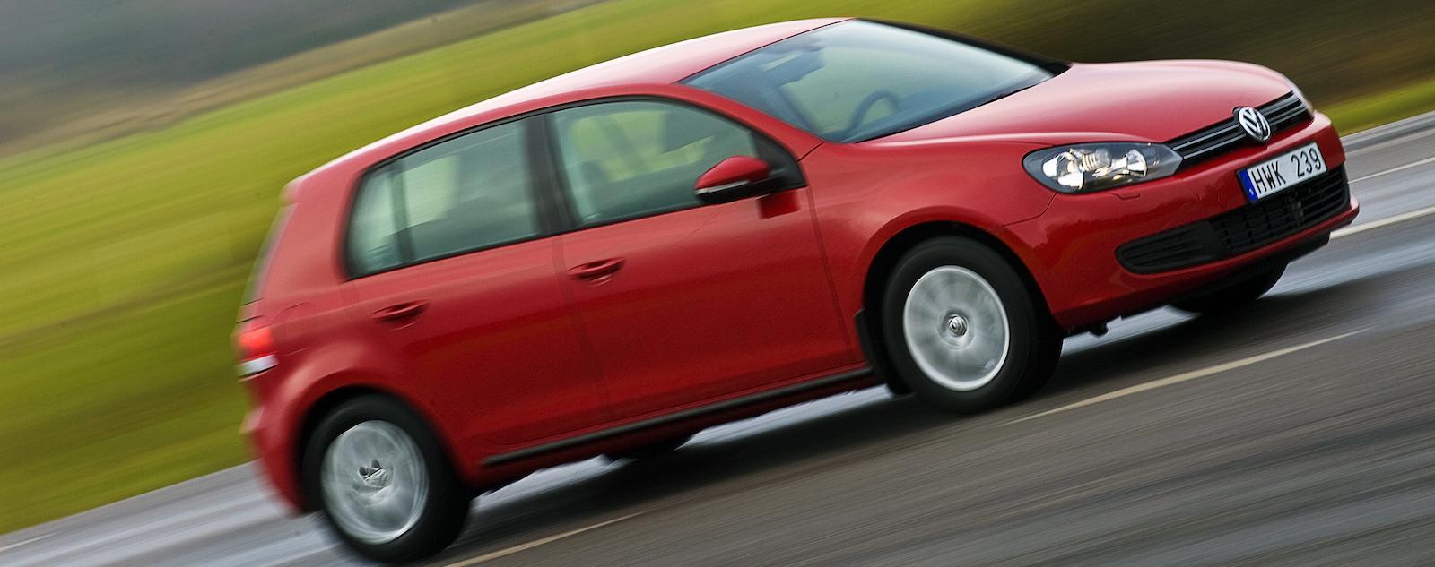 En röd Volkswagen Golf kör på en blöt väg. (AI text)