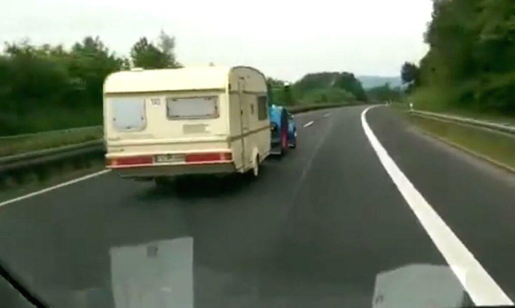 En bil körer längs en motorväg med ett släp bakom sig. (AI text)