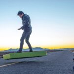 En man cyklar på en skateboard längs en ökenväg. (AI text)