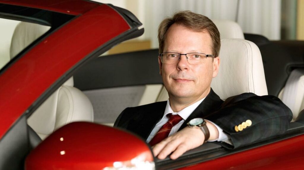 En man i kostym sitter i förarsätet av en röd sportbil. (AI text)