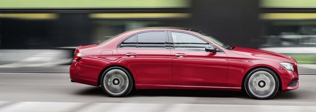 En röd Mercedes-Benz C-klass sedan kör ner en stadsgata. (AI text)