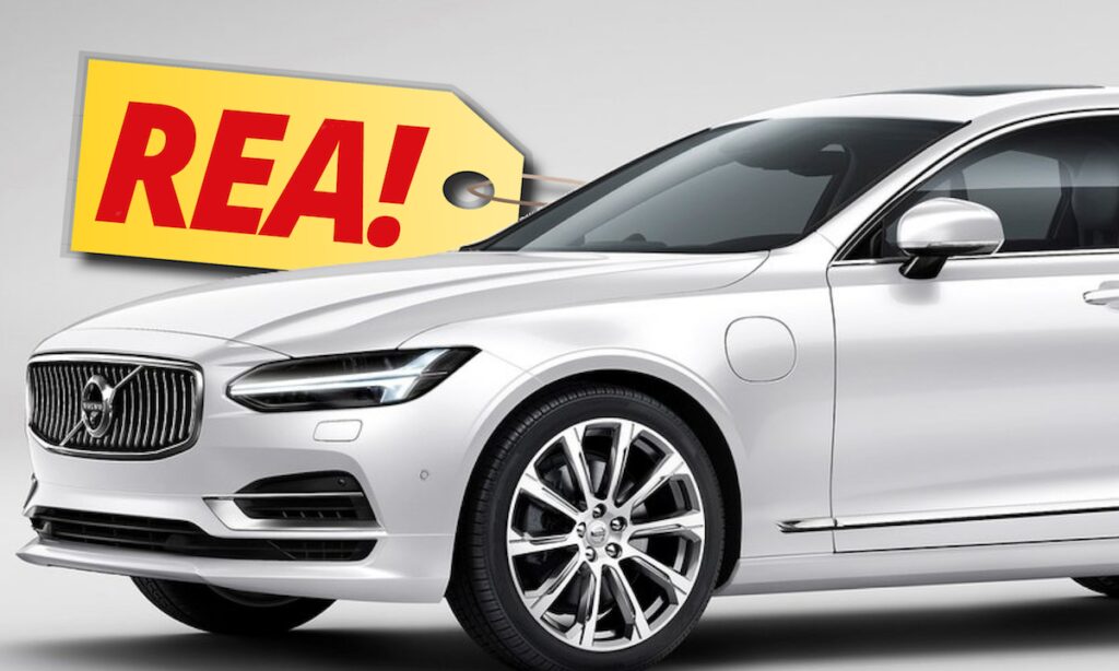 En vit Volvo S90 sedan med en REA-bilskiltag. (AI text)