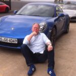 En man sitter på marken bredvid en grupp bilar. (AI text)