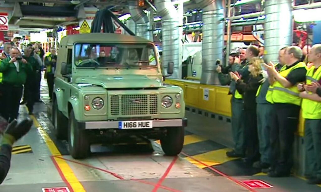 En grupp personer står sammanlagt kring en bil. (AI text)