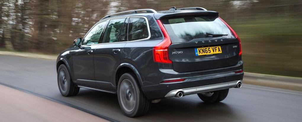 En Volvo XC90 SUV kör längs en landsväg. (AI text)