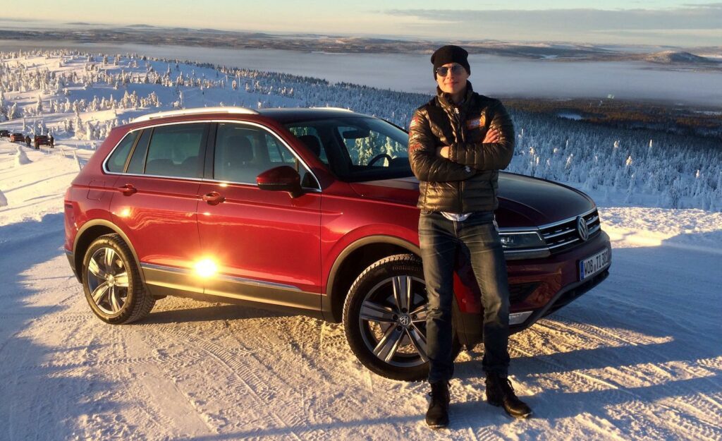 En man står bredvid en röd Volkswagen SUV i snön. (AI text)