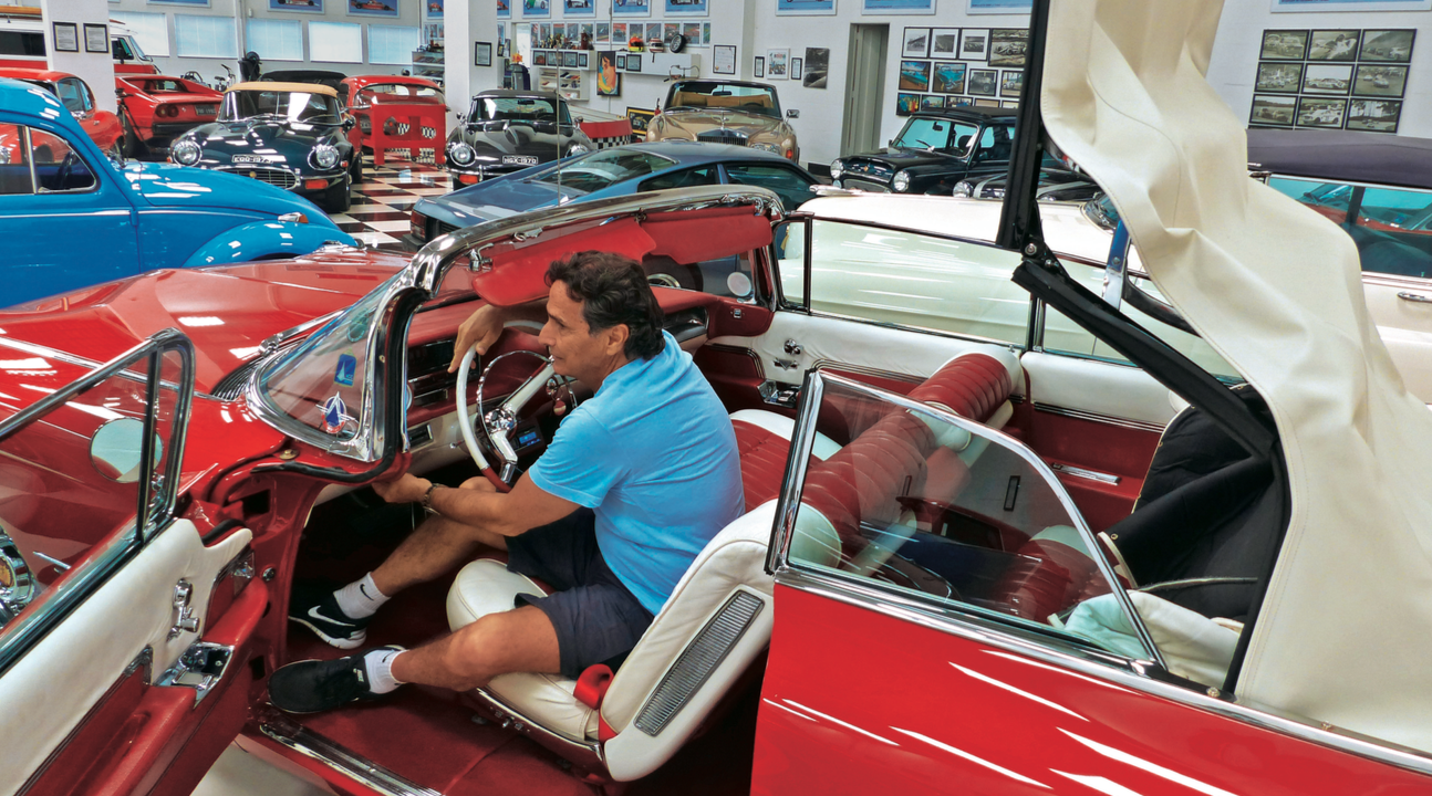 En man sitter i en röd bil i en garage. (AI text)