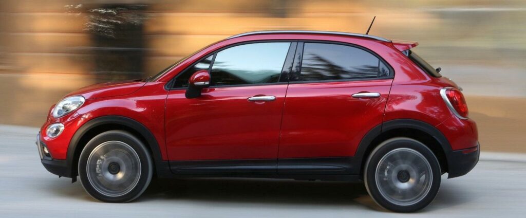 En röd Fiat 500 kör nedför en stadsgata. (AI text)