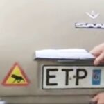 En man monterar en bilregistreringsplåt på en bil. (AI text)