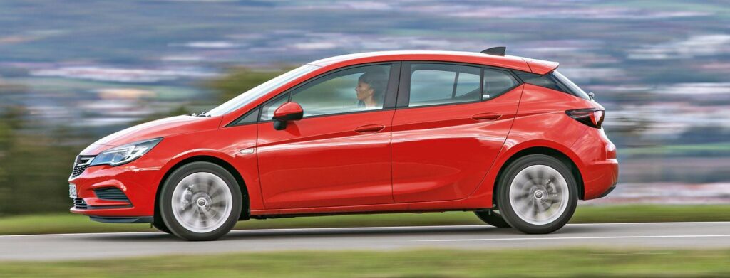 En röd Chevrolet Acadia kör nerför en landsväg. (AI text)