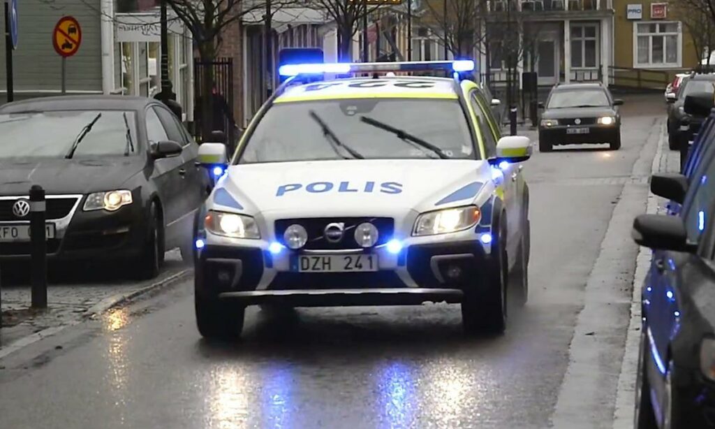 En polisbil kör längs en gata i en stad. (AI text)