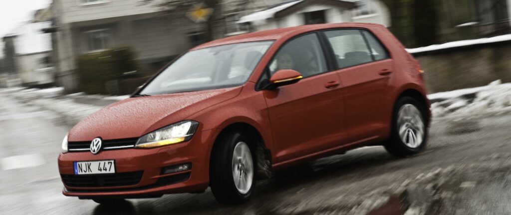 En Volkswagen Golf kör nedför en gata. (AI text)