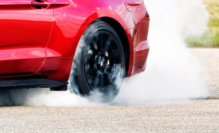 En röd Ford Mustang kör nerför vägen med rök som kommer ut. (AI text)