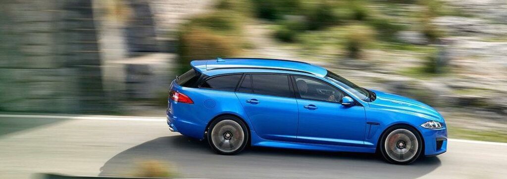 En blå Jaguar XF kör nedför en bergsväg. (AI text)