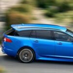 En blå Jaguar XF kör nedför en bergsväg. (AI text)