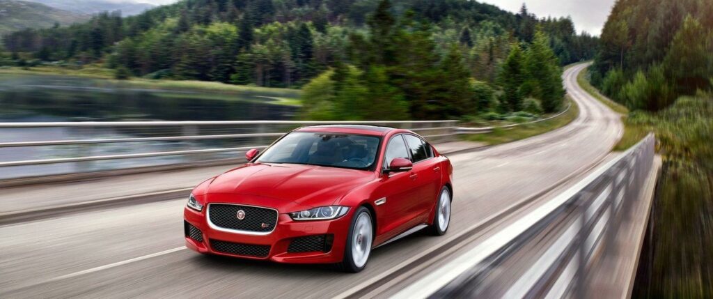 En röd Jaguar XF körs nedför en bergsväg. (AI text)