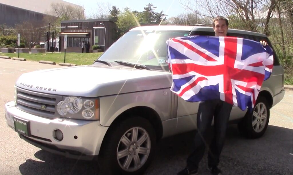 En man håller en brittisk flagga framför en Land Rover. (AI text)